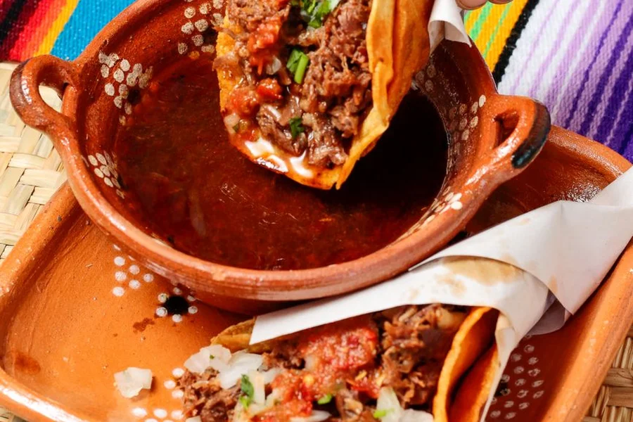 Platter of crispy quesabirria street tacos with cilantro, lime, and rich beef dipping broth